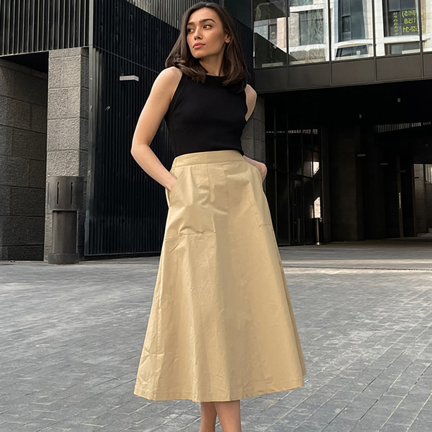 Donna con gonna beige e top nero davanti a edificio moderno. Moda urbana, abbigliamento elegante, look casual chic.