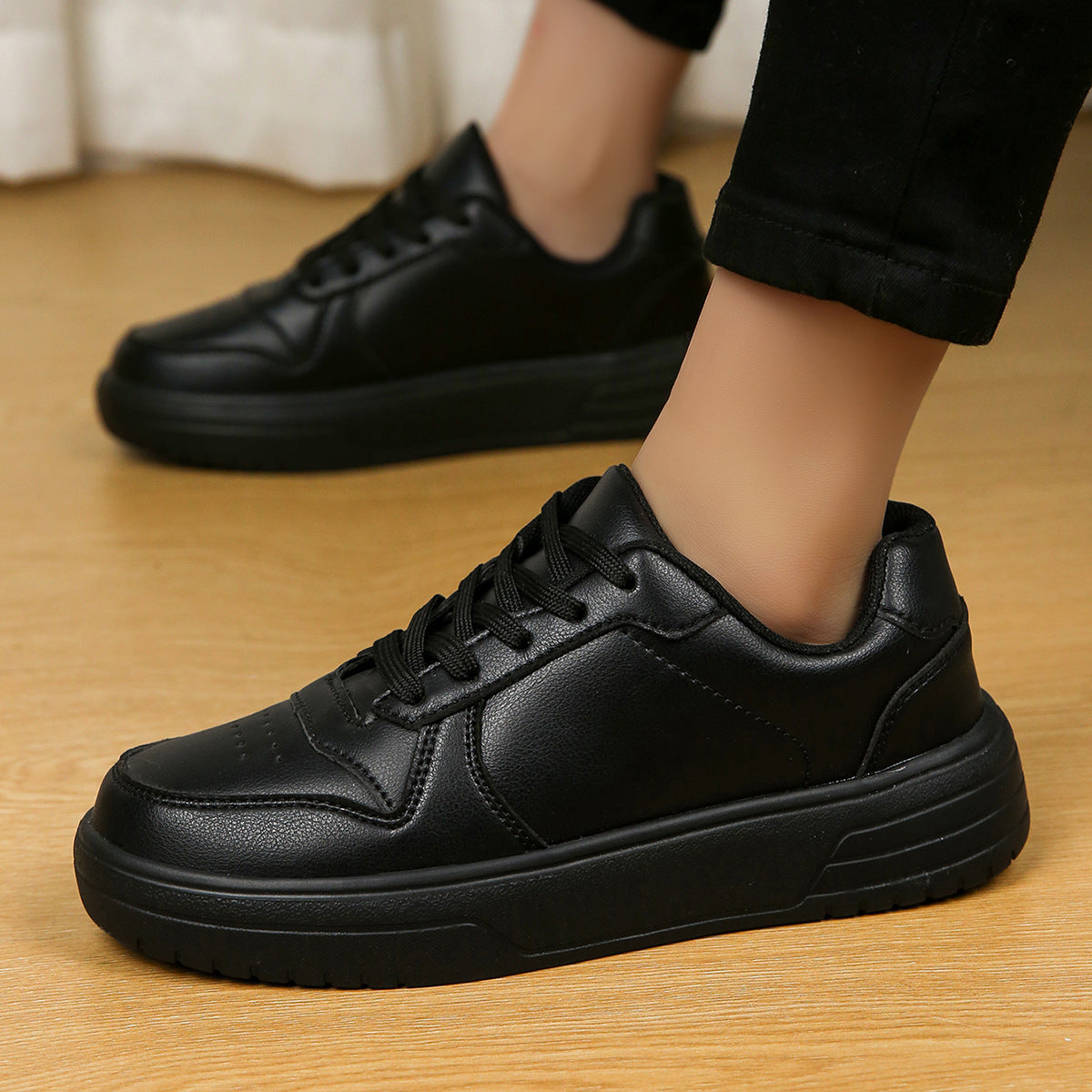Scarpe da ginnastica nere in pelle, design moderno, suola spessa, indossate su pavimento in legno. Scarpe casual eleganti per uomo o donna.