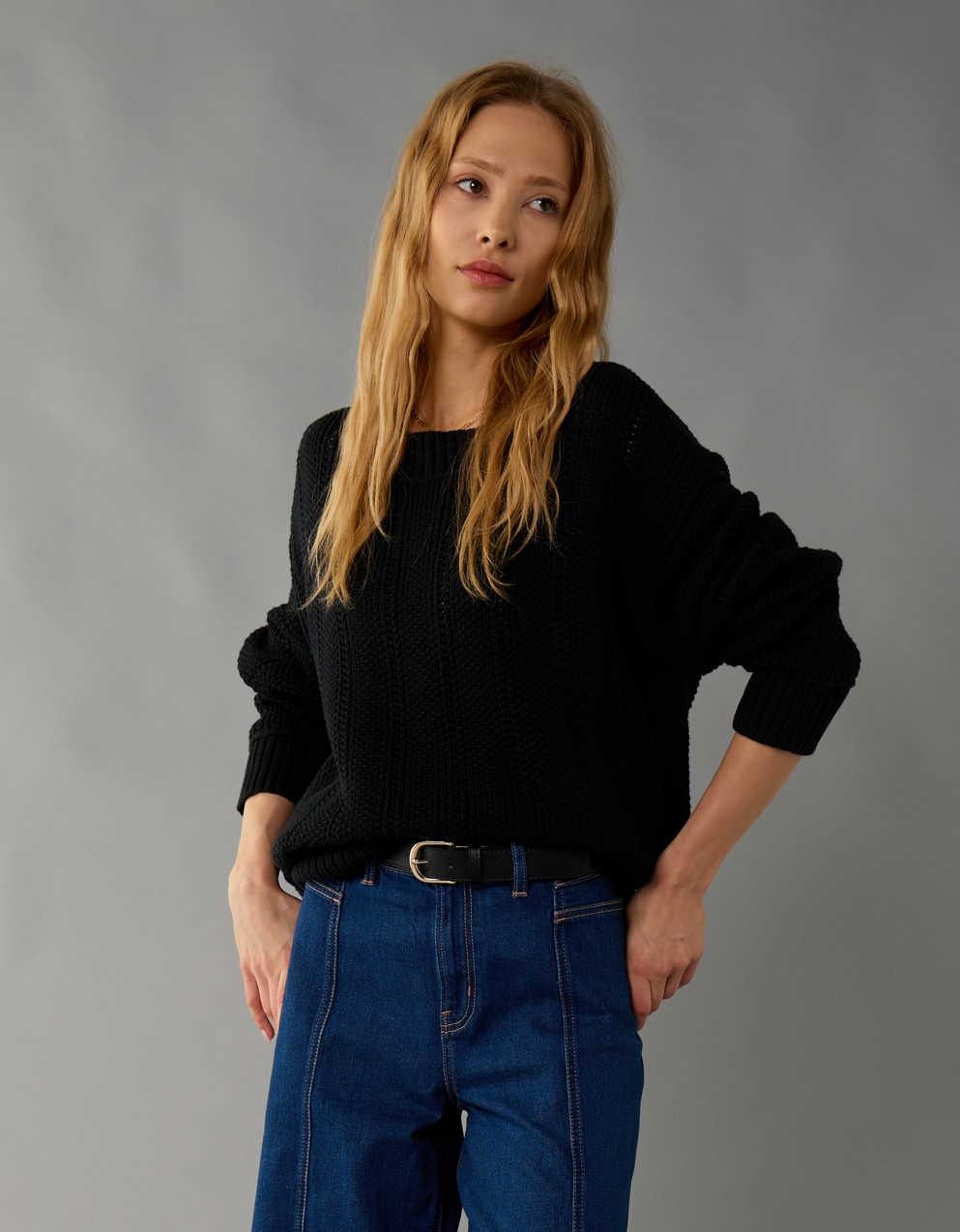 Donna con maglione nero e jeans blu, posa su sfondo grigio. Moda casual autunnale, abbigliamento femminile, stile moderno.