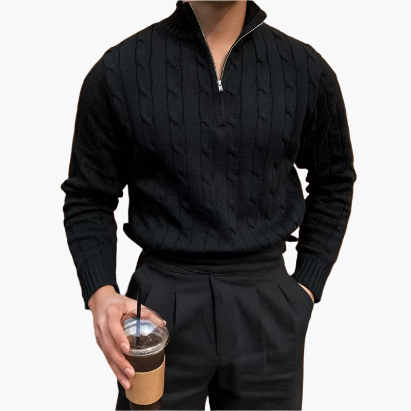 Uomo con maglione nero a trecce e zip, pantaloni neri, tiene in mano un bicchiere di caffè freddo. Moda maschile elegante e casual.