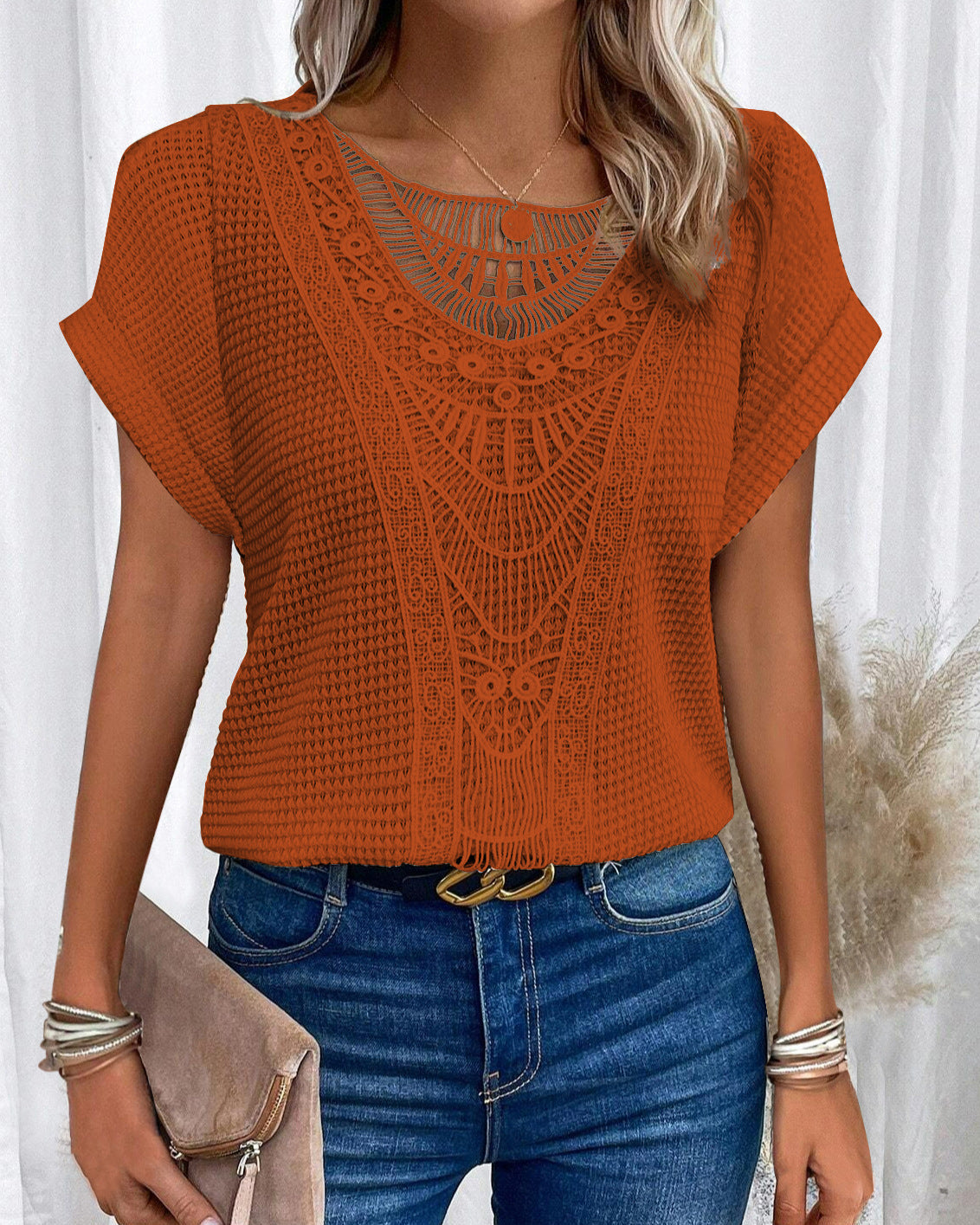 Donna con maglia arancione traforata, jeans blu e accessori argento. Moda estiva, abbigliamento casual elegante, stile boho chic.