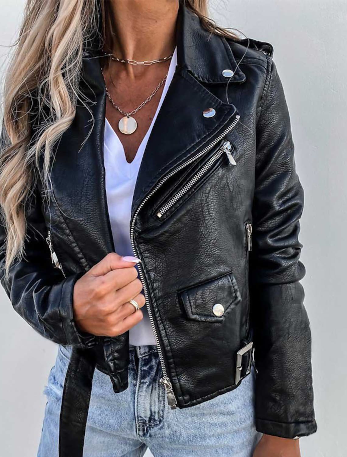 Donna con giacca di pelle nera, maglietta bianca e jeans chiari. Stile casual, moda autunnale, accessori con collane a catena.