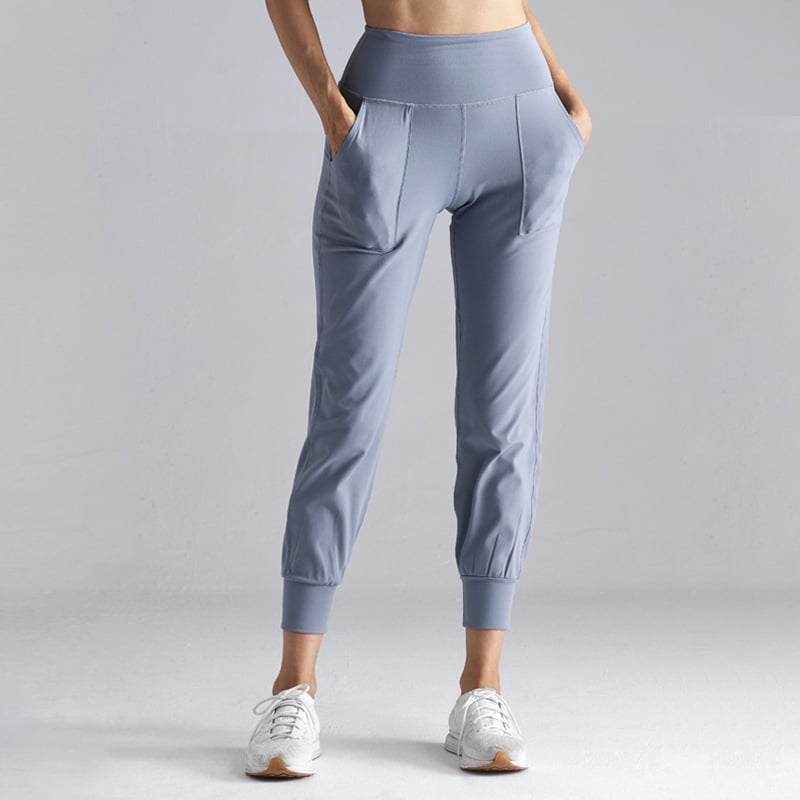 Pantaloni sportivi donna grigi, vita alta, tasche laterali, abbinati a scarpe da ginnastica bianche. Abbigliamento fitness comodo ed elegante.