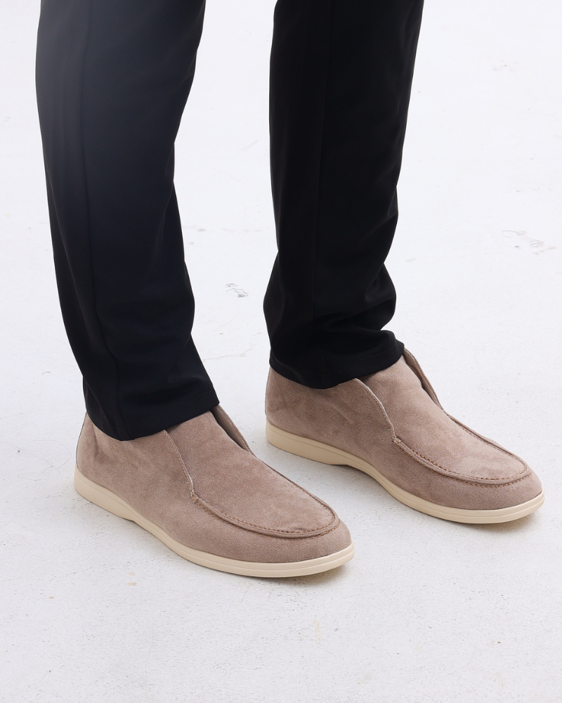 Scarpe mocassini beige in pelle scamosciata su pavimento bianco, indossate con pantaloni neri. Eleganti calzature uomo, moda casual chic.