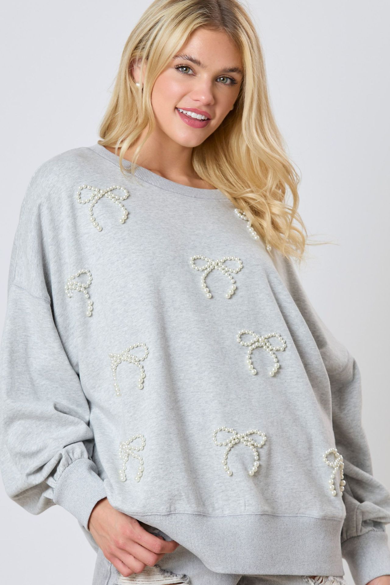 Donna bionda con maglione grigio decorato con fiocchi di perle, moda casual, abbigliamento autunnale, stile elegante, tendenza femminile.