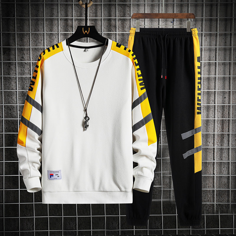 Tuta sportiva uomo bianca e nera con dettagli gialli, felpa a maniche lunghe e pantaloni con scritte, appesa su griglia metallica.