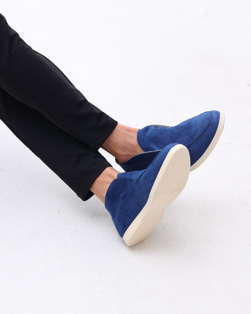 Scarpe mocassini blu in camoscio su sfondo bianco, indossate con pantaloni neri. Eleganti e moderne, ideali per moda maschile casual.