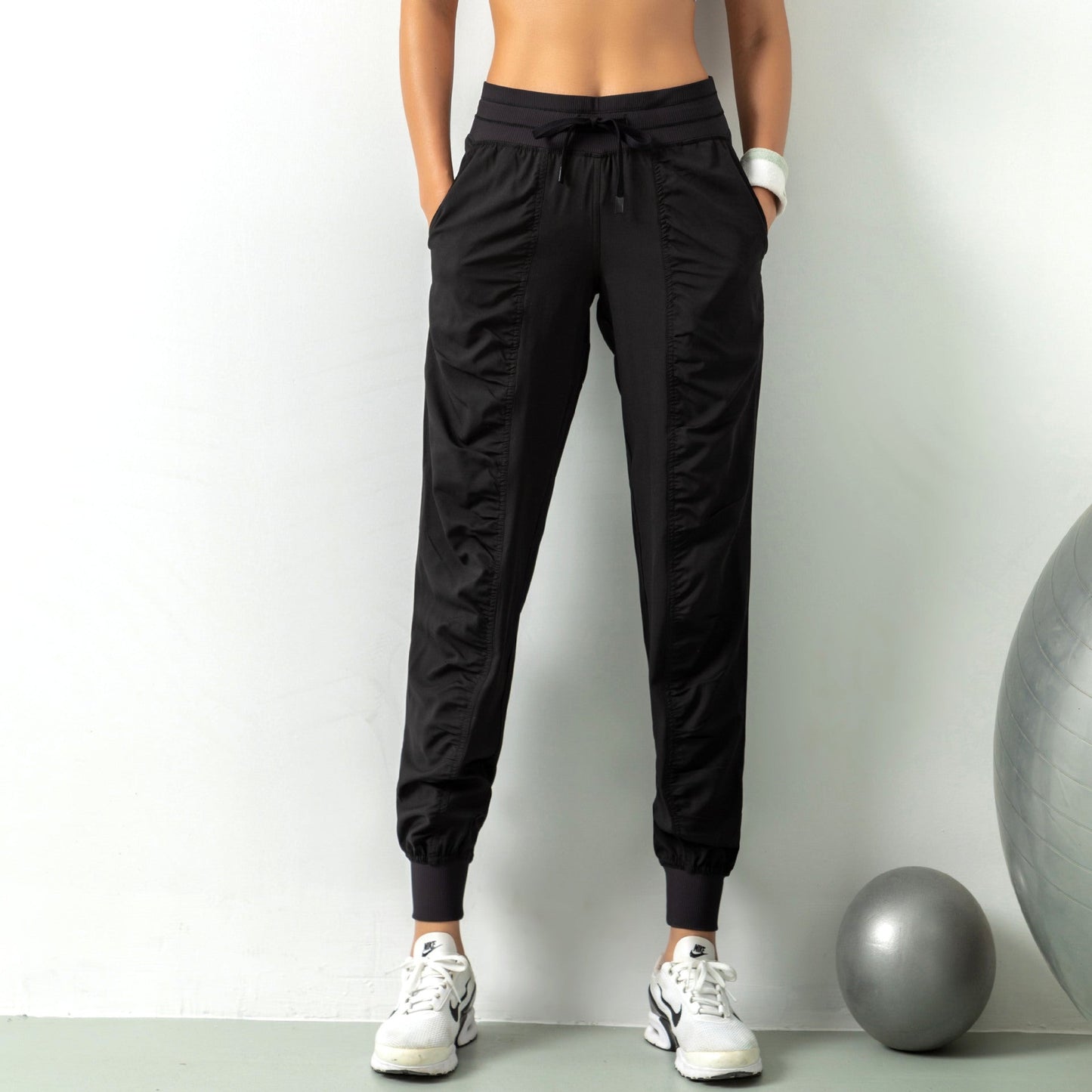 Pantaloni sportivi neri da donna, con tasche e coulisse, indossati con scarpe da ginnastica bianche. Fitness, moda sportiva, abbigliamento comodo.
