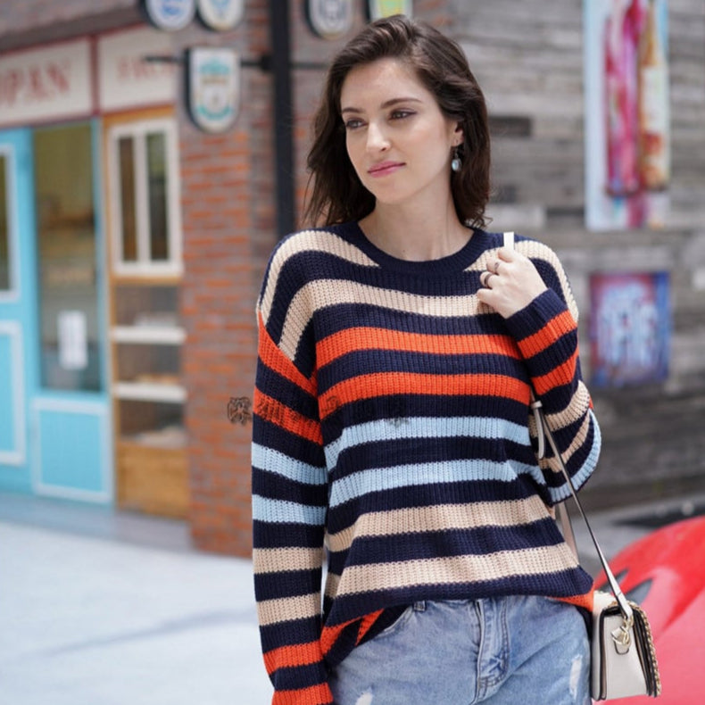Donna con maglione a righe colorate e jeans strappati, passeggia in un ambiente urbano. Moda casual autunnale, look trendy e moderno.