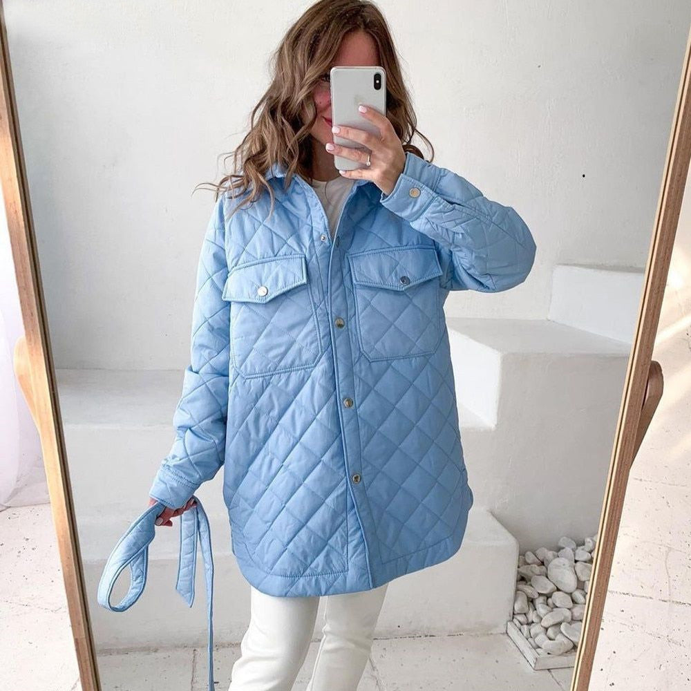 Donna con giacca trapuntata azzurra, smartphone in mano, scatta selfie. Moda invernale, abbigliamento casual, stile moderno.