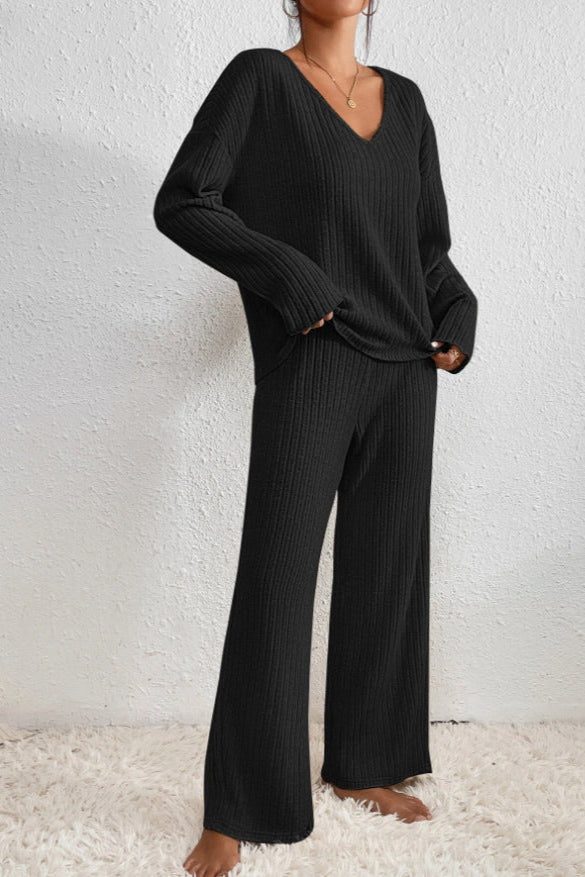 Donna in completo maglia nero, maglione a V e pantaloni larghi, su tappeto bianco. Moda autunnale, abbigliamento casual elegante.
