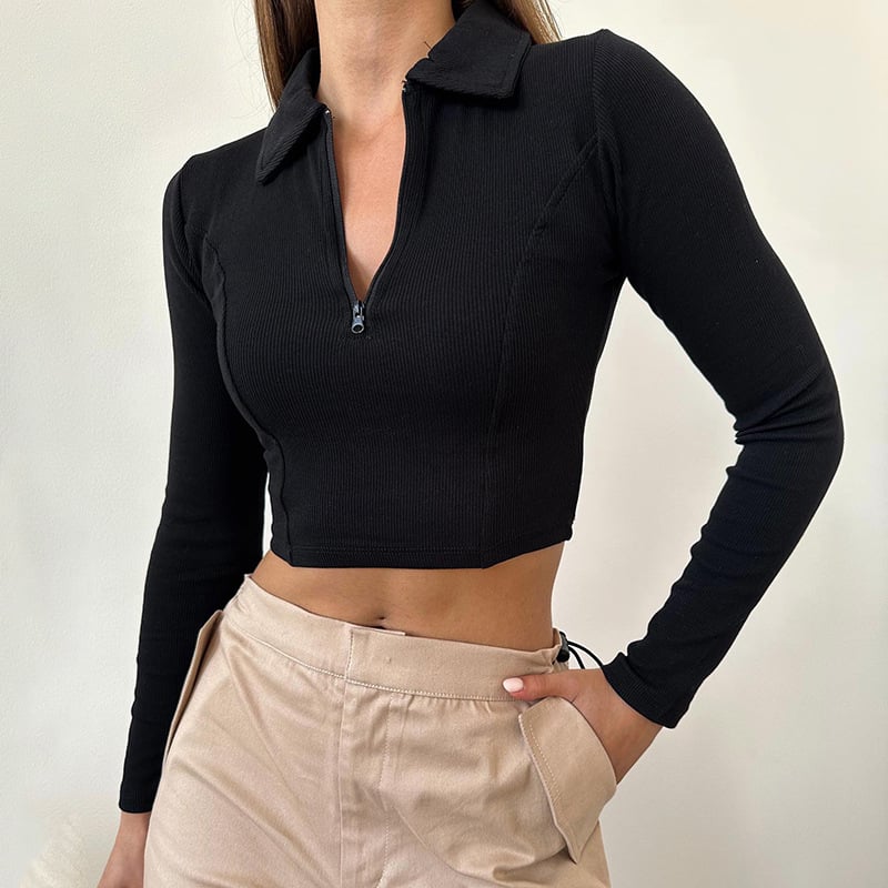 Donna indossa maglia nera a maniche lunghe con zip, abbinata a pantaloni beige. Moda casual, abbigliamento femminile, stile autunnale.