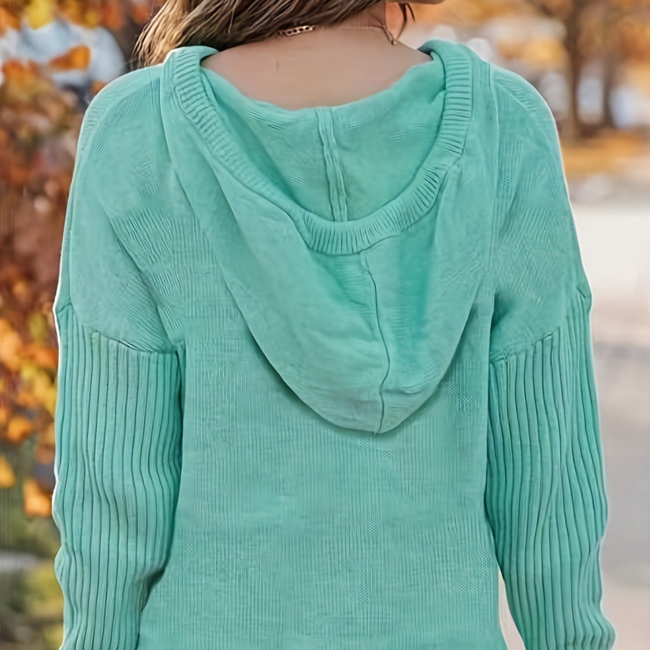 Donna con maglione verde menta con cappuccio, vista di spalle, in un ambiente autunnale. Maglione casual, moda autunno, abbigliamento femminile.