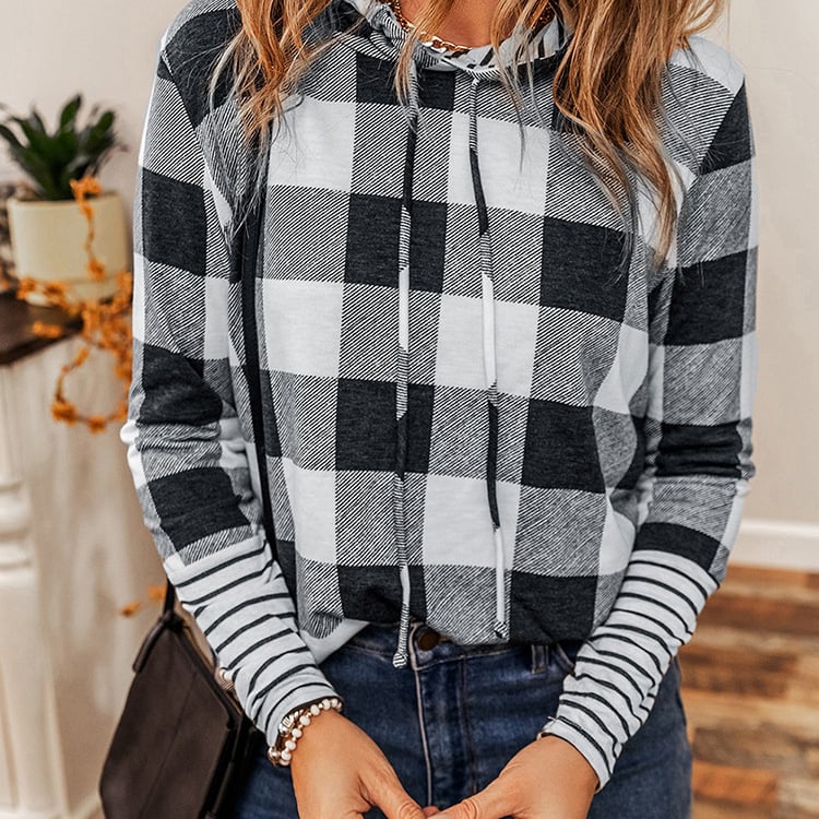 Donna con felpa a quadri bianco e nero, maniche a righe, in un ambiente interno. Stile casual, moda autunnale, outfit femminile trendy.