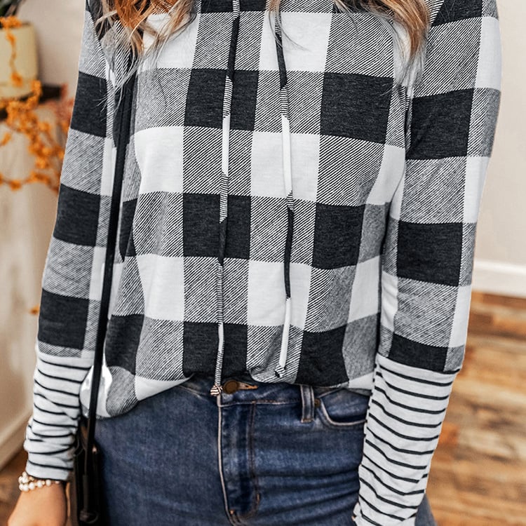 Donna con maglia a quadri bianco e nero, jeans blu, in un ambiente interno. Moda autunno, abbigliamento casual, stile moderno.