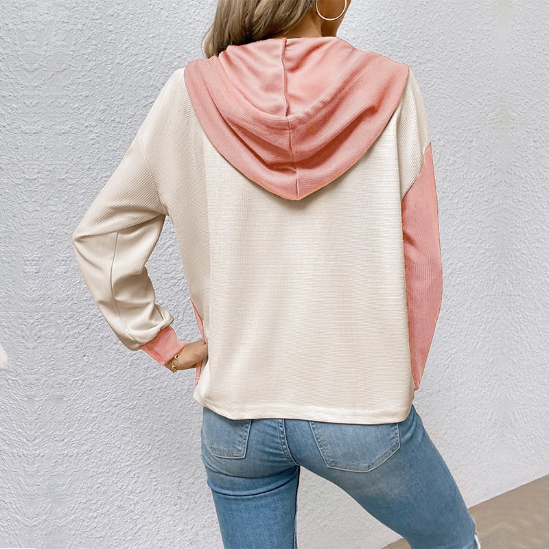 Donna con felpa bicolore beige e rosa, cappuccio, maniche lunghe, jeans aderenti. Moda casual femminile, abbigliamento autunnale trendy.