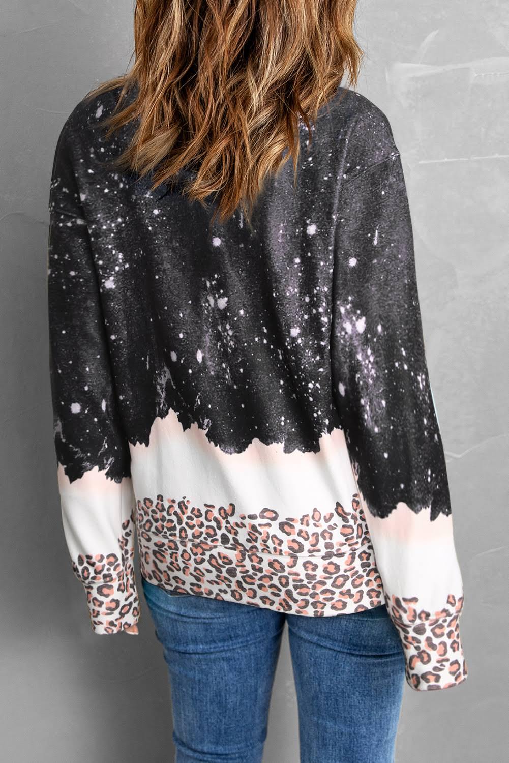 Donna di spalle indossa maglione con stampa galassia e leopardata, jeans blu. Moda casual autunno, abbigliamento trendy, stile urbano.
