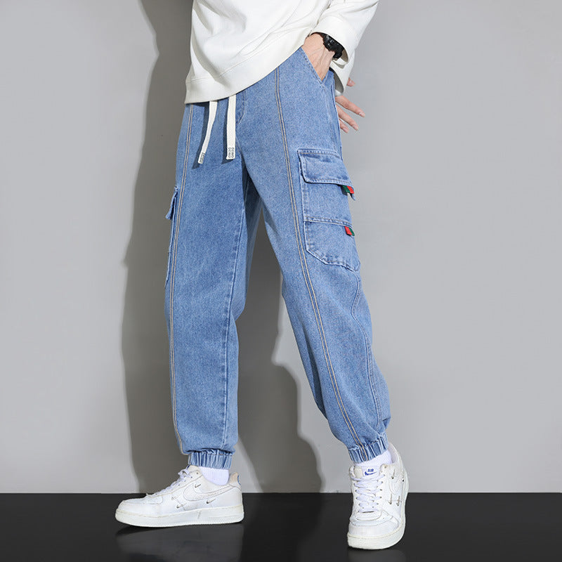 Pantaloni cargo in denim blu con tasche laterali, indossati con sneakers bianche e felpa bianca. Stile casual e moderno per uomo.
