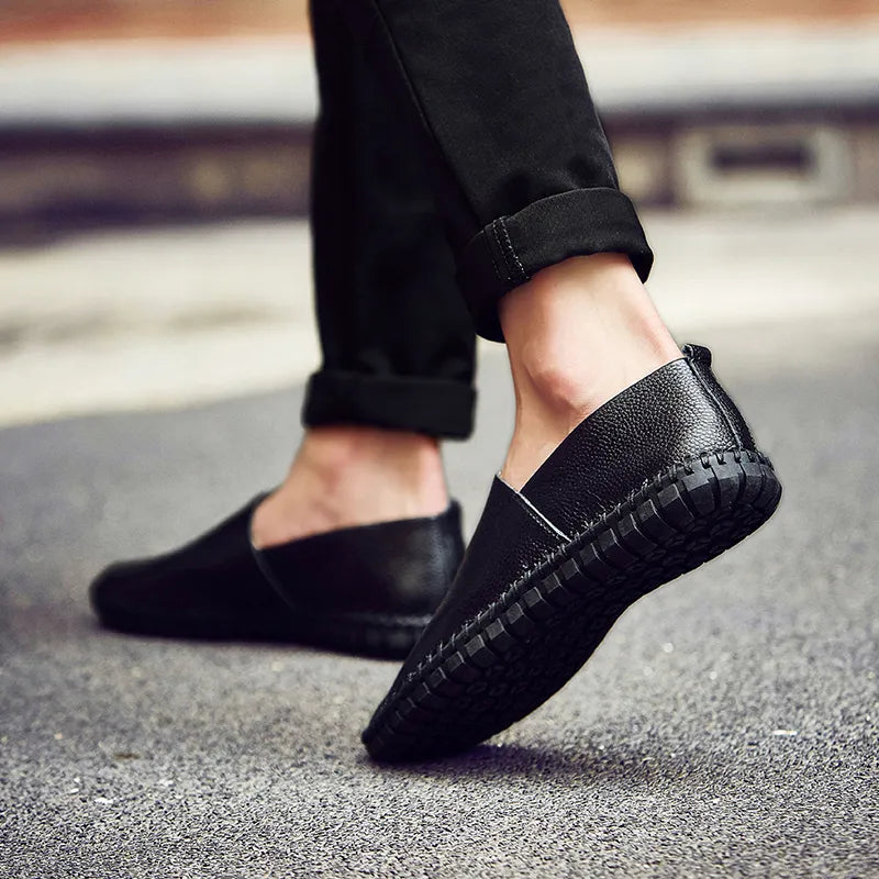 Scarpe mocassini uomo in pelle nera, suola antiscivolo, indossate su strada asfaltata. Eleganti e casual, ideali per moda urbana.