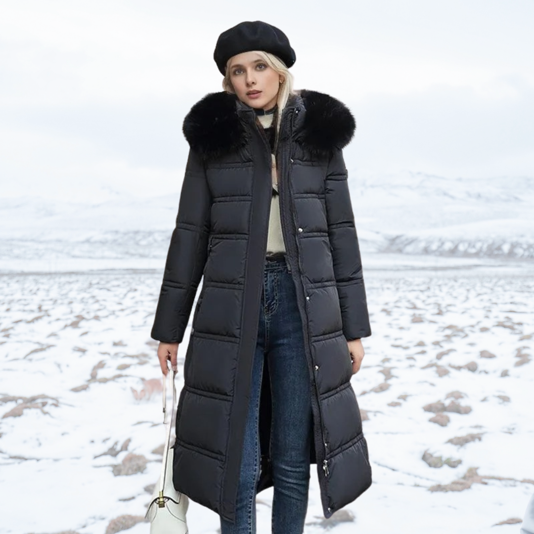 Donna in cappotto lungo nero con cappuccio in pelliccia, berretto nero, jeans, in un paesaggio innevato. Moda invernale, abbigliamento caldo.