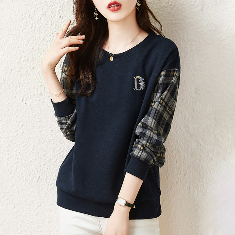 Donna con maglia blu scuro, maniche a quadri, posa contro muro bianco. Moda casual autunnale, abbigliamento femminile elegante, stile moderno.