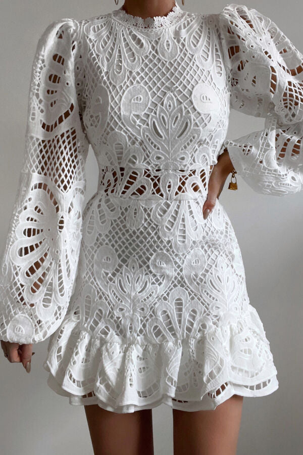 Abito bianco in pizzo con maniche lunghe a sbuffo, motivo floreale e dettagli traforati. Elegante e femminile, ideale per eventi speciali.