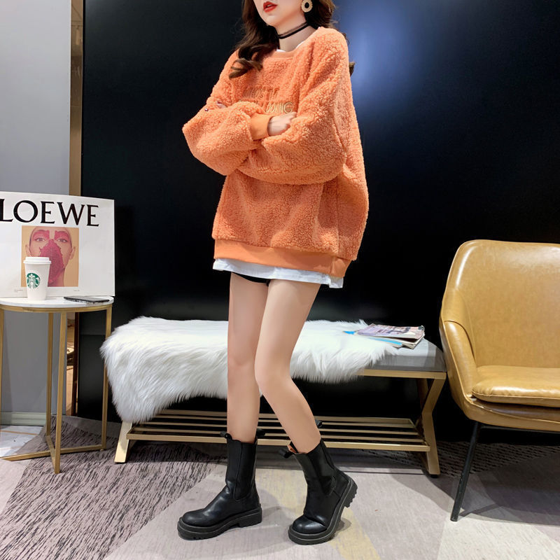 Donna con maglione arancione oversize, stivali neri e minigonna bianca in un salotto moderno. Moda autunnale, abbigliamento casual chic.