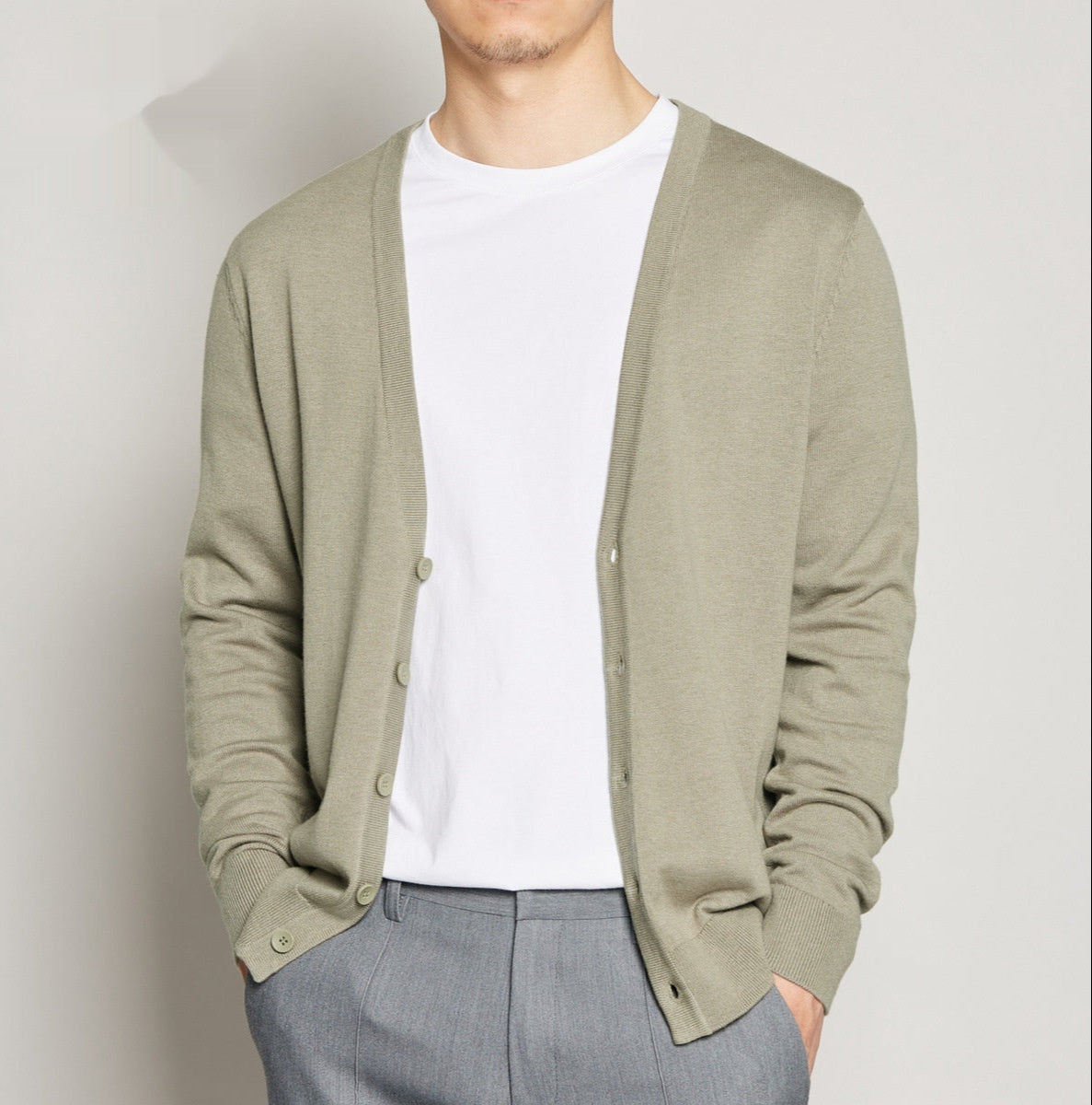 Uomo con cardigan beige aperto su maglietta bianca e pantaloni grigi. Moda maschile casual, abbigliamento elegante, stile minimalista.