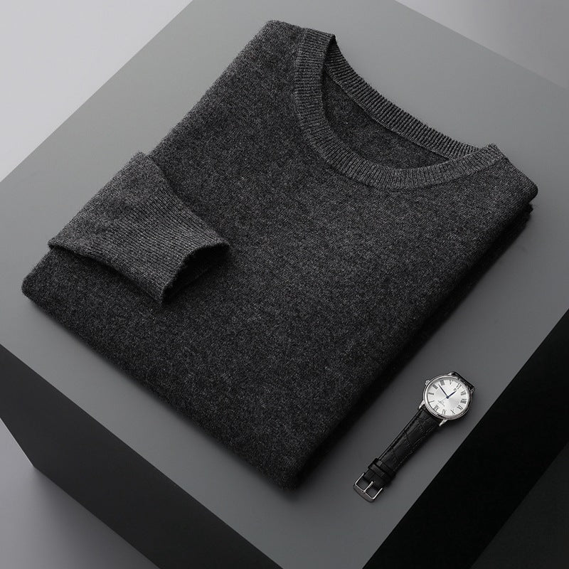 Maglione grigio in cashmere piegato su tavolo nero, accanto a orologio da polso elegante con cinturino in pelle nera. Moda uomo, abbigliamento invernale.