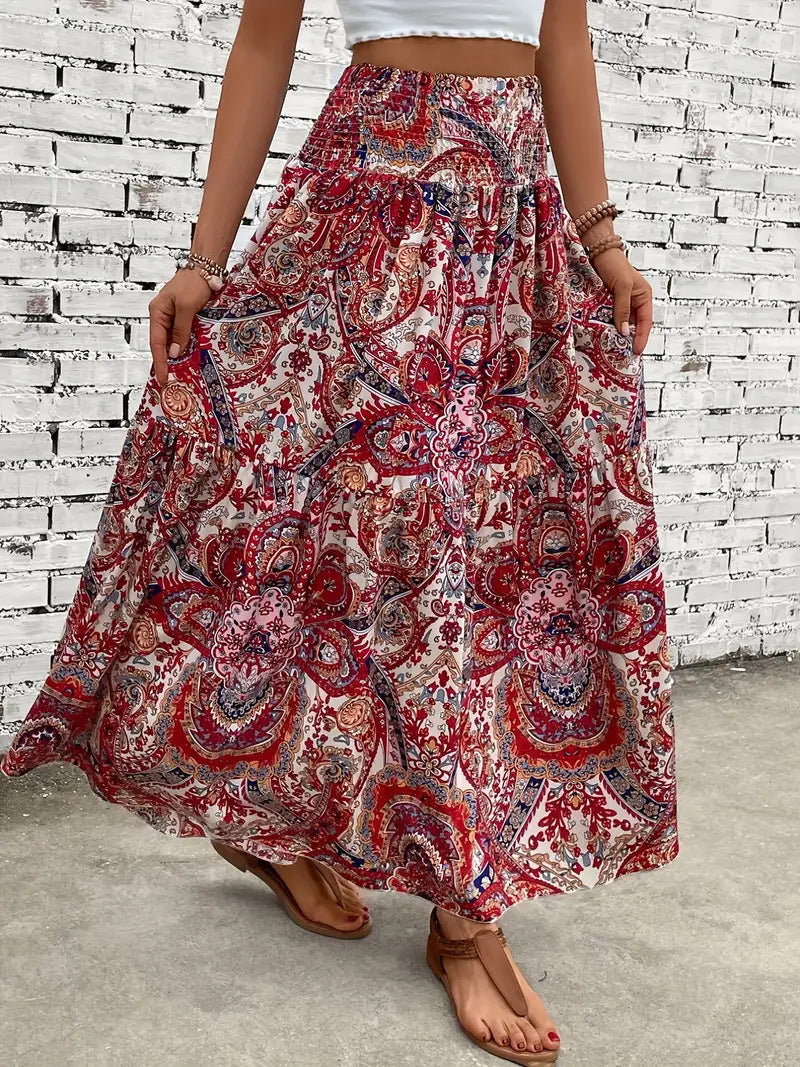 Gonna lunga boho a fiori rossi e rosa, indossata da donna con top bianco, sfondo muro di mattoni bianchi. Stile estivo, moda casual.