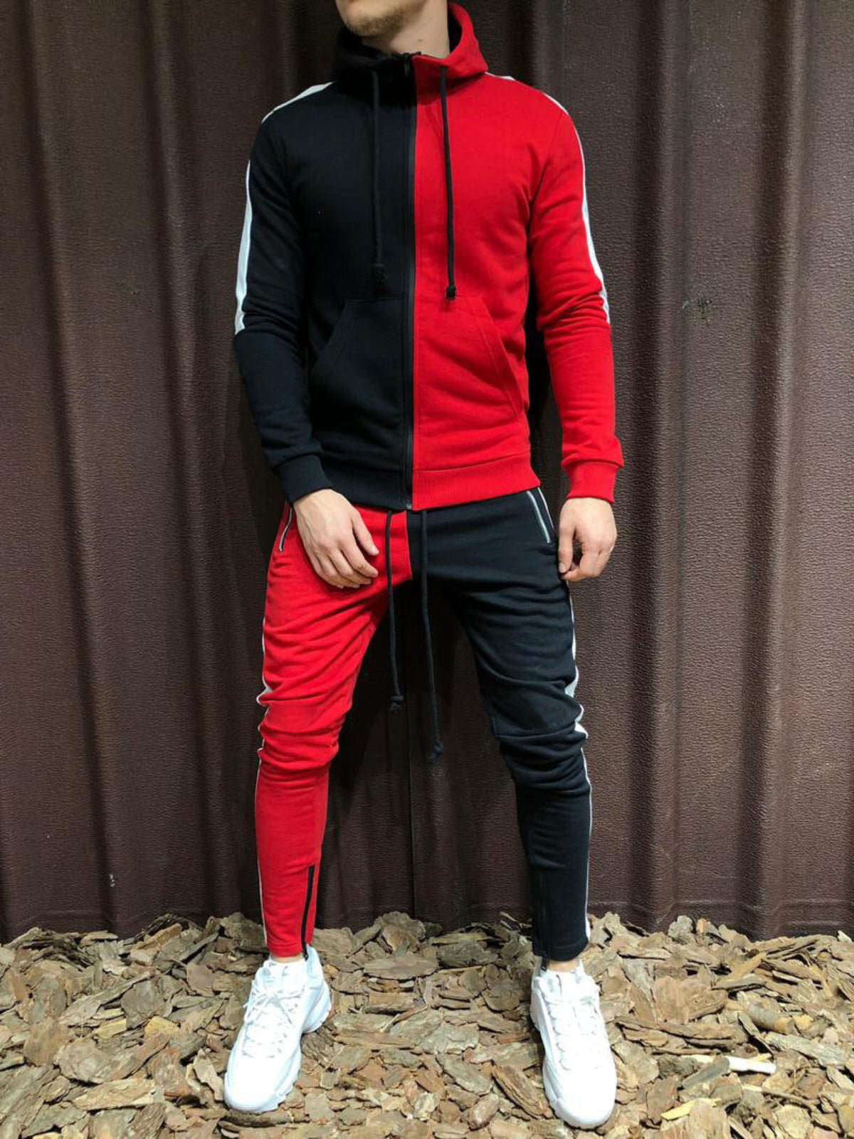 Tuta sportiva uomo bicolore rosso e nero, con cappuccio e pantaloni abbinati, su sfondo marrone. Stile casual, moda streetwear.