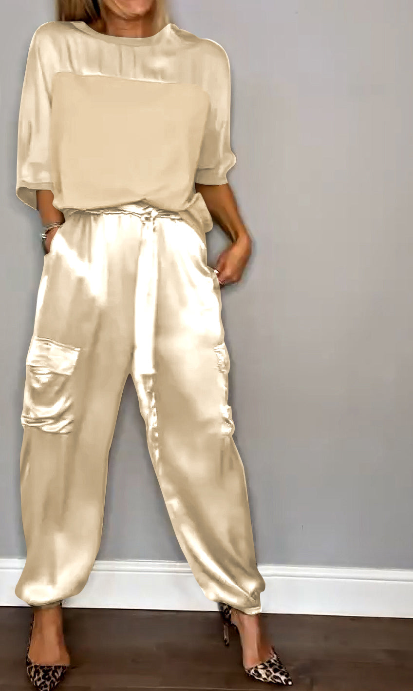 Donna in abbigliamento elegante color crema, indossa pantaloni di seta con tasche e top coordinato, scarpe leopardate. Moda femminile chic.