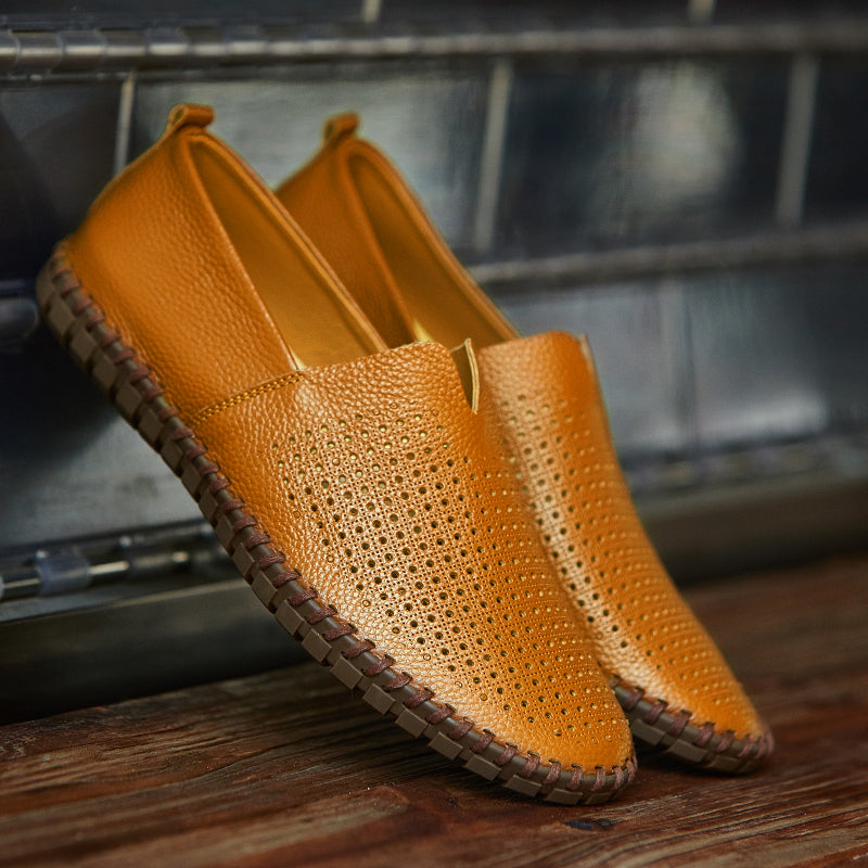 Scarpe mocassini in pelle gialla traforata, suola in gomma marrone, appoggiate su una superficie di legno. Eleganti e casual, ideali per l'estate.