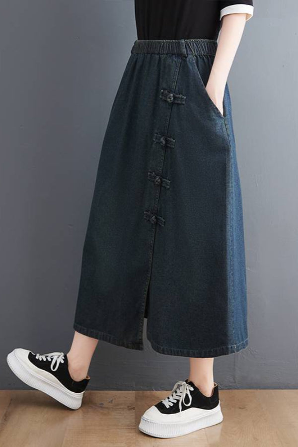 Gonna lunga in denim blu con bottoni decorativi, tasche laterali, abbinata a scarpe da ginnastica bianche e nere. Moda casual donna.