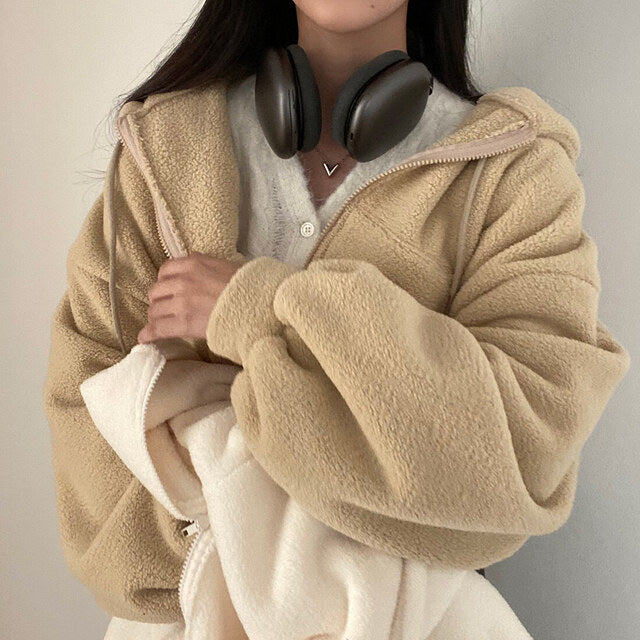 Donna con giacca in pile beige, cuffie nere al collo, maglione bianco. Moda autunnale, abbigliamento casual, comfort e stile.