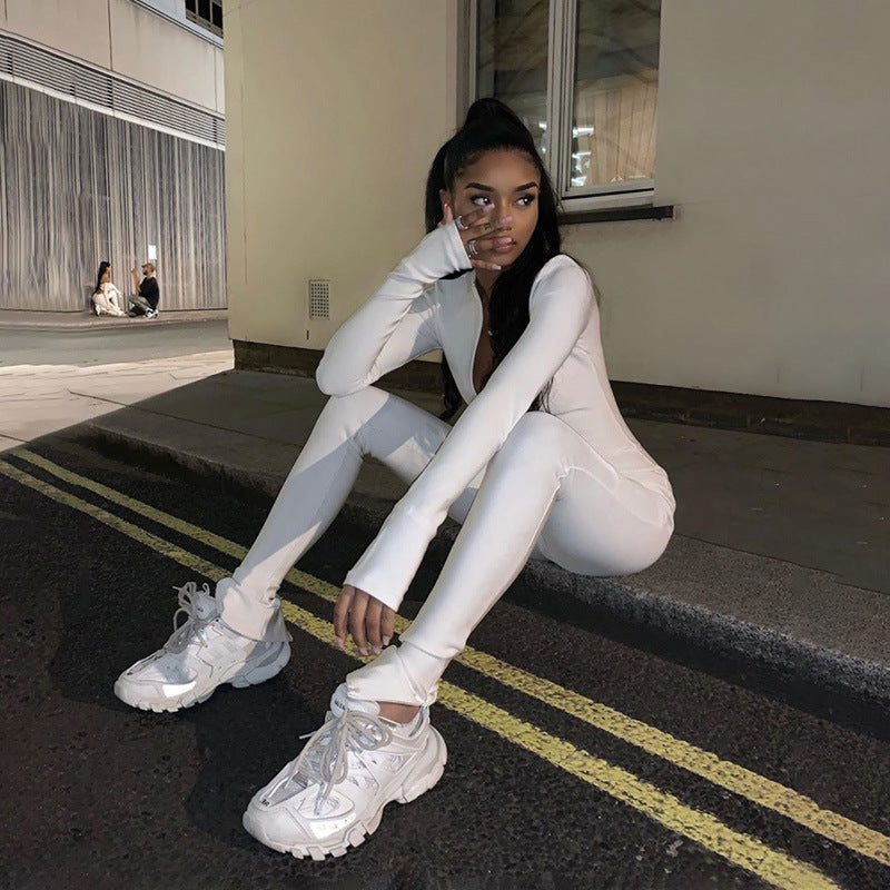 Giovane donna seduta su un marciapiede di notte, indossa tuta bianca e sneakers, riflettendo. Moda urbana, abbigliamento casual, stile streetwear.