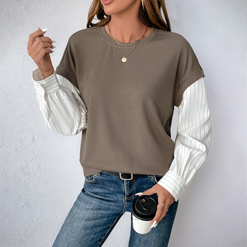 Donna con maglia marrone a maniche lunghe a righe bianche, jeans blu, collana dorata, tiene una tazza di caffè. Moda casual autunnale.