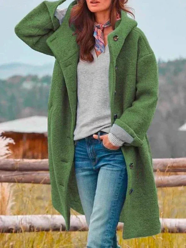 Donna con cappotto verde oversize, jeans e maglione grigio, posa all'aperto. Moda autunnale, stile casual, sciarpa colorata.