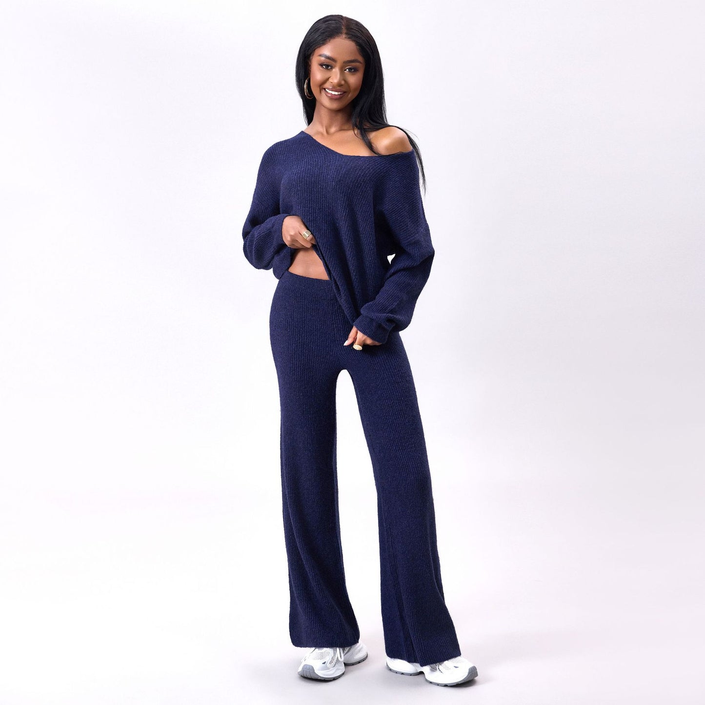 Donna sorridente in abbigliamento casual blu, maglione e pantaloni coordinati, posa su sfondo bianco. Moda donna, outfit comodo, stile autunnale.
