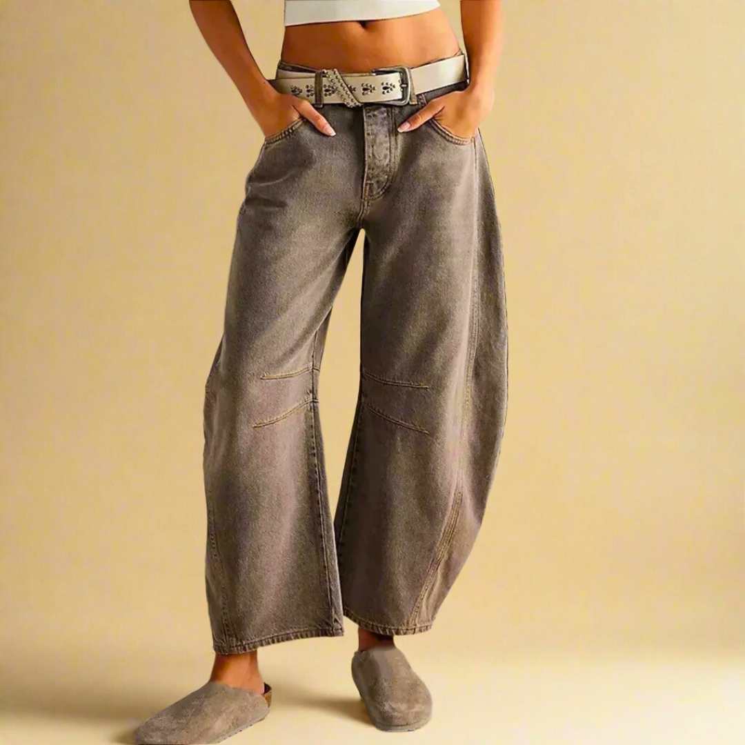 Jeans larghi grigi a vita alta, con cintura bianca e scarpe abbinate, indossati da una persona su sfondo beige. Moda casual, stile contemporaneo.