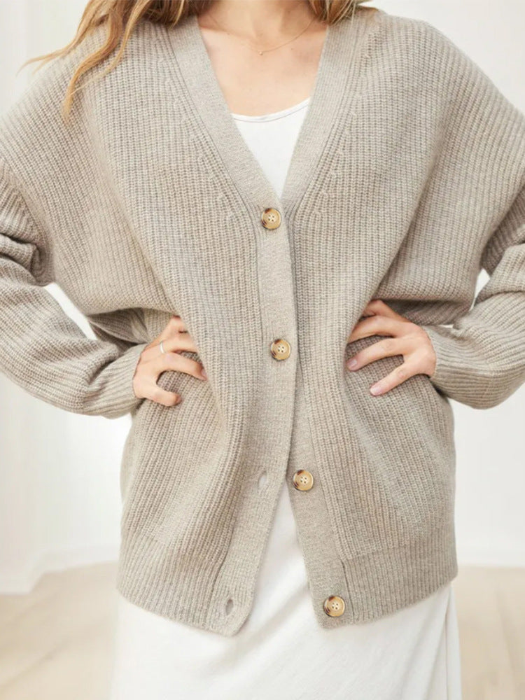 Donna indossa cardigan beige oversize in maglia con bottoni in legno, abbinato a vestito bianco. Moda autunnale, abbigliamento casual elegante.