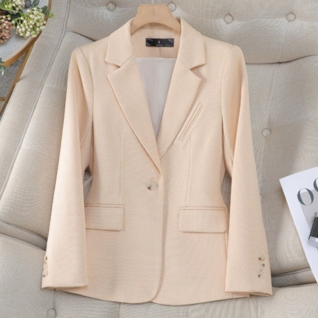 Giacca elegante beige da donna su divano, stile classico con bottoni e tasche, perfetta per abbigliamento formale e business casual.