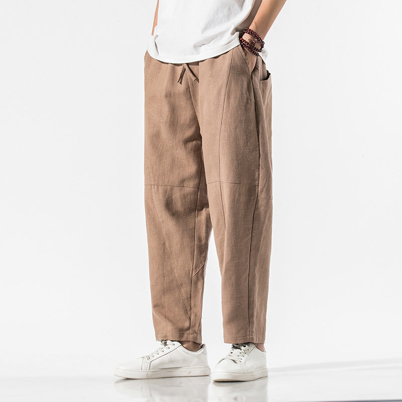 Pantaloni larghi uomo in lino marrone, stile casual, con tasche laterali. Indossati con t-shirt bianca e scarpe da ginnastica bianche.
