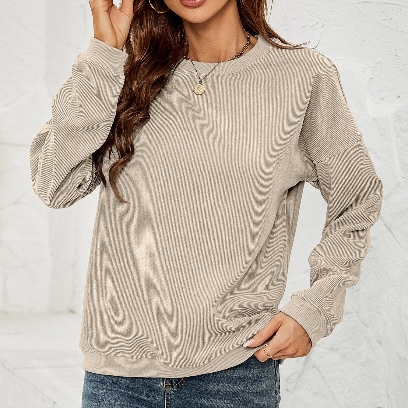 Donna con maglione beige a coste, maniche lunghe, indossa jeans e collana dorata. Moda casual autunnale, abbigliamento femminile trendy.