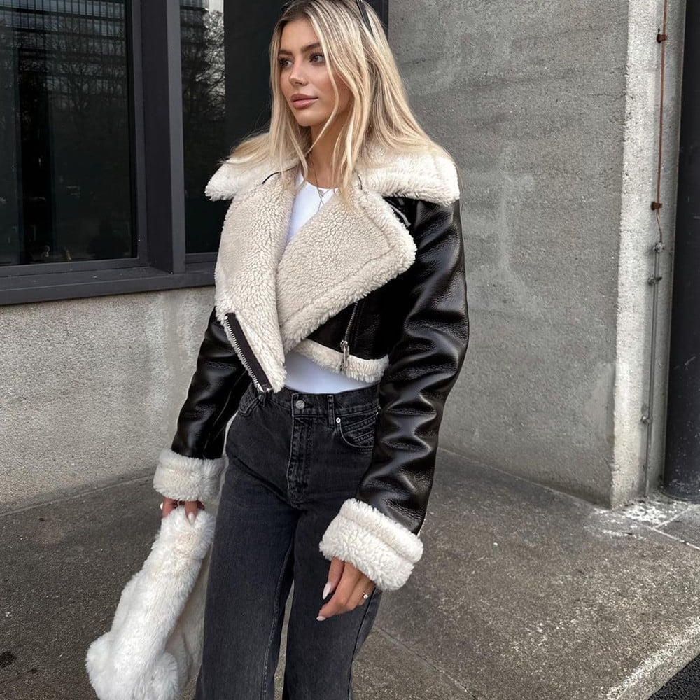 Donna con giacca in pelle nera e pelliccia bianca, jeans neri, posa all'aperto. Moda invernale, stile casual chic, tendenze abbigliamento 2023.