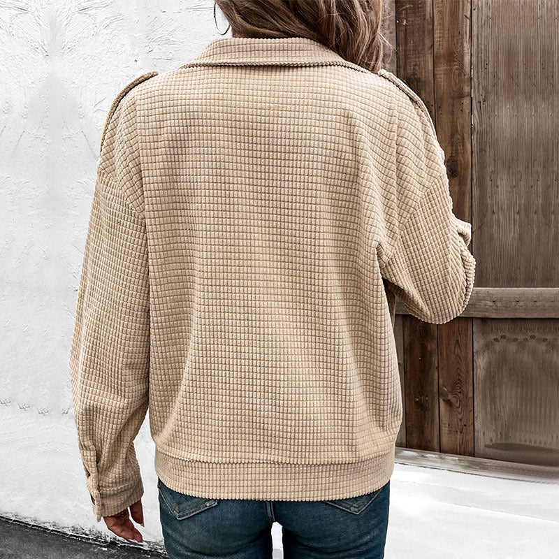 Giacca beige a quadri, stile casual, indossata da una persona di spalle. Tessuto morbido, ambientazione esterna con porta in legno.