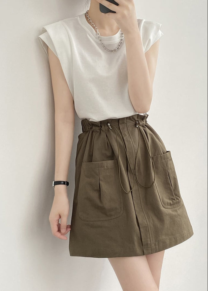 Donna in posa con maglietta bianca e gonna verde oliva con tasche grandi, stile casual chic. Accessori: collana argento, bracciale nero.