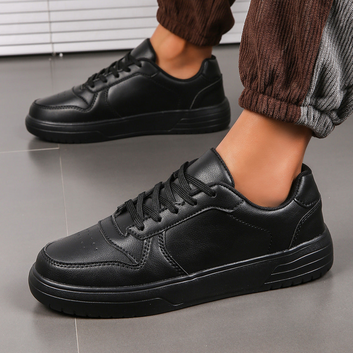 Scarpe da ginnastica nere in pelle, indossate da una persona su pavimento grigio. Design moderno, suola robusta, perfette per look casual e sportivo.