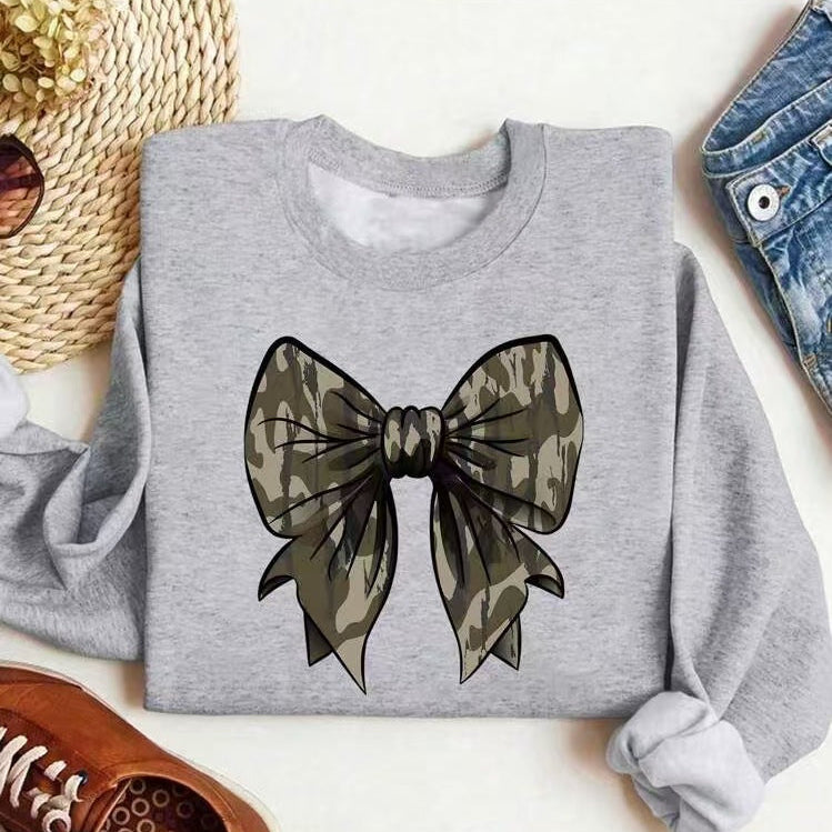 Maglietta grigia con stampa fiocco mimetico, affiancata da cappello di paglia, occhiali da sole e jeans. Moda casual, stile urbano.