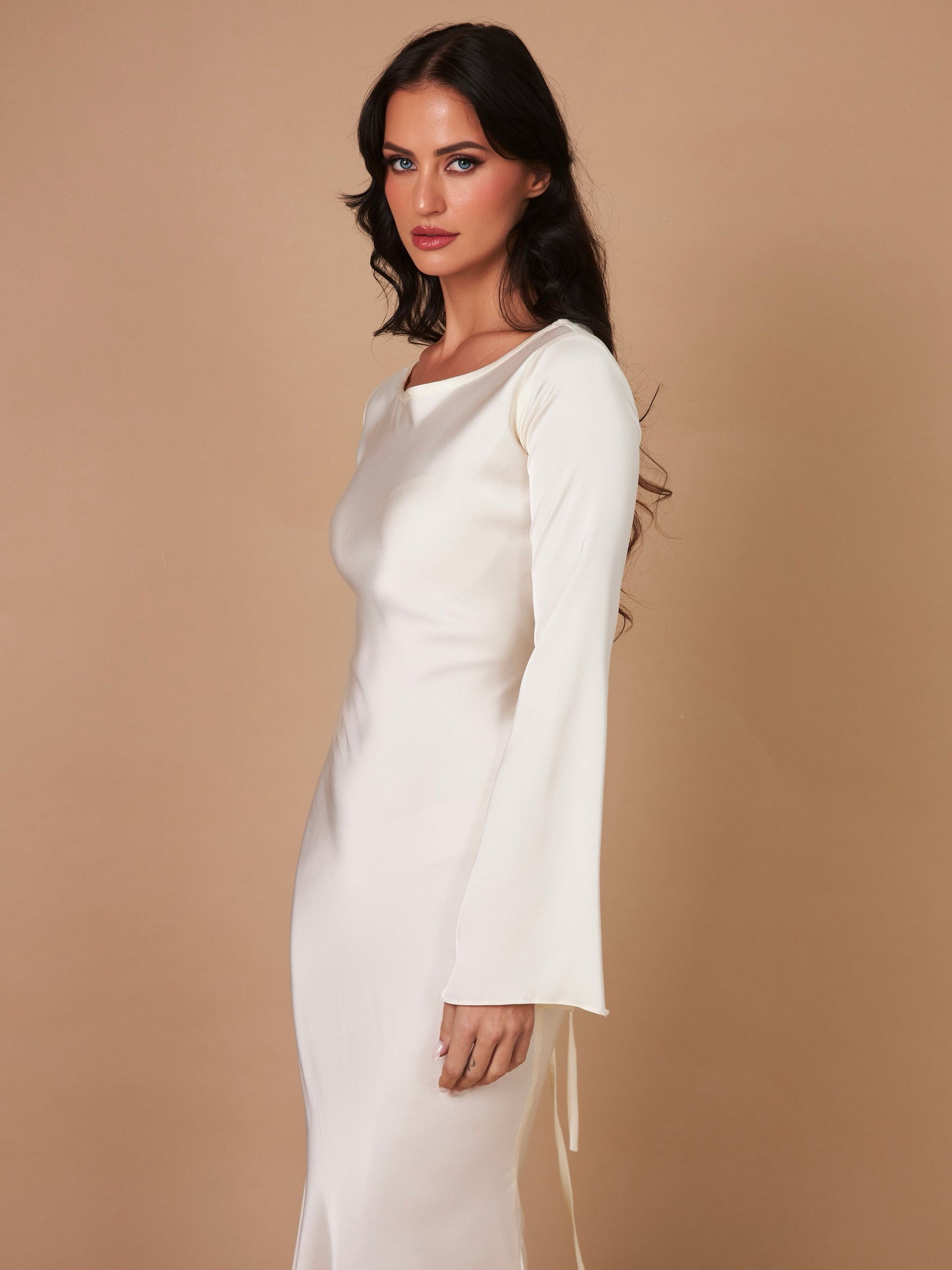 Donna in abito bianco elegante con maniche lunghe, sfondo beige. Moda femminile, abbigliamento formale, stile sofisticato.